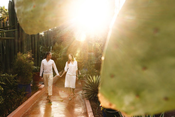 Sun shines over couple in white closes walking around the botanic garden in African city - obrazy, fototapety, plakaty