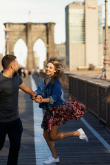 Fototapeta premium Beautiful young man and woman pose on the Brooklyn Bridge in the rays of morning sun
