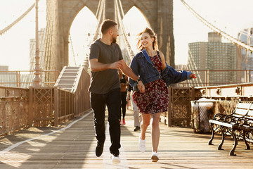Beautiful young man and woman pose on the Brooklyn Bridge in the rays of morning sun
