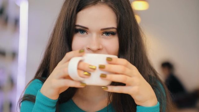 Woman enjoying drinking coffee holding cup sitting in cafe