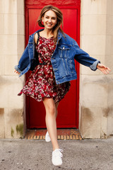 Cheerful girl dressed in denim style jumps before a red door