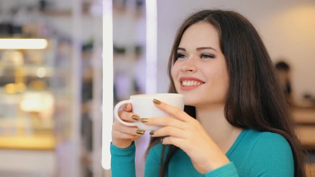 Smiling girl enjoying drinking coffee holding cup sitting in cafe