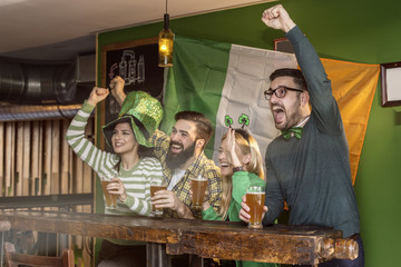 Group of four fun friends looking sports match on tv with beer on Irish traditiona pub