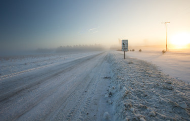 Naklejka premium Winter Driving Background. Rural country snow covered road with a frigid winter wind blowing snow across the horizon.