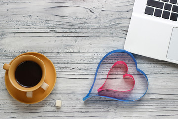 Background of a valentine on a wooden table with a laptop cup of coffee hearts beside a napkin for writing. Valentine's Day.