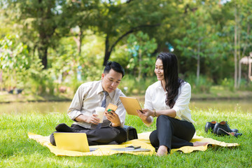 couple business man and woman relaxing in park by using smart phone and tablet