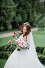Fototapeta na wymiar Stunning bride in luxury dress holds in her hands pink wedding bouquet standing in a green park