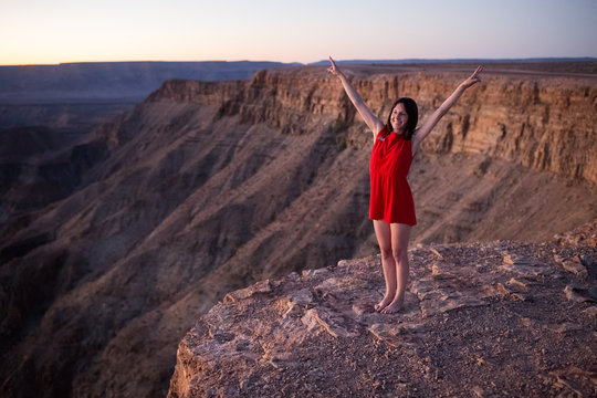 Young woman in bright red dress standing on the edge of a mounta