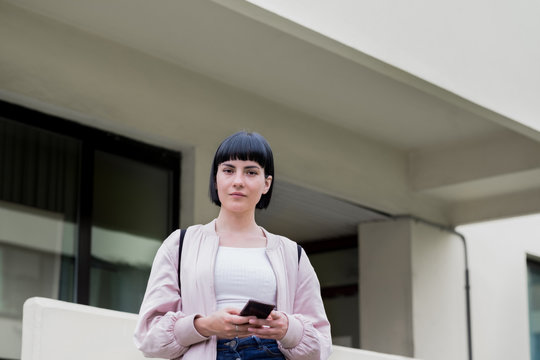 Portrait of a young female model using her phone in front of the building