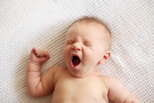 Newborn baby boy yawning while lying on the bed