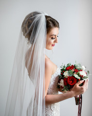 Gorgeous bride in classy dress poses with a red wedding bouquet of roses and peonies