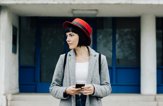 Portrait of a young female model with red hat using her phone in front of the building