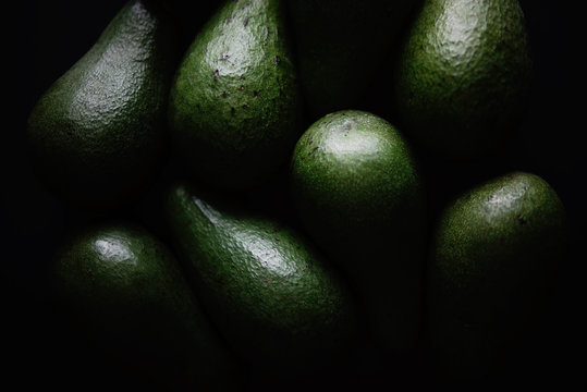 Avocados on a dark background in subdued light.