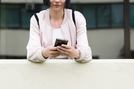 Portrait of a young anonymous female model using her phone in front of the building