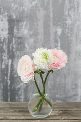 Vase with beautiful bouquet of ranunculus flowers on wooden table. rustic background with copy space. Close up Persian buttercup flower.