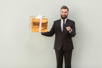 Businessman holding gift box, pointing fingers at camera and smiling