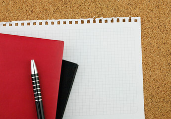 Black and red notebooks on the clean white sheet with black pen on the cork board background;...