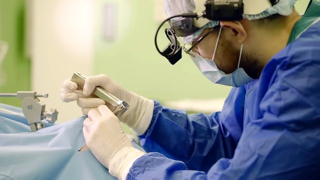 male surgeon is inspecting cavity of the larynx of patient is lying on an operating table under anesthesia