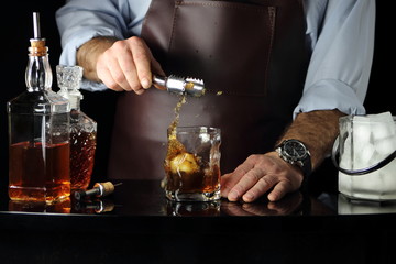 мужчина бросает в стакан с виски кубик льда