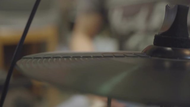 Drummer fastly jamming on an electric hi-hat cymbal in foregound.