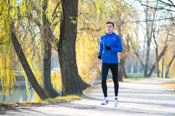 Fototapeta premium Young Sports Man Running in the Park in Cold Sunny Autumn Morning. Healthy Lifestyle and Sport Concept.