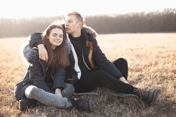 Young woman and young man sitting on the grass in the field under sunlight.