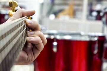 The guitarist's hand, close-up and soft focus, takes the akrod on a guitar fretboard, against the background of the drum set.