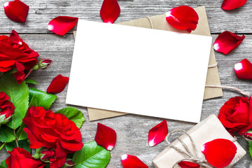 blank white greeting card with red rose flowers bouquet and envelope with petals and gift box
