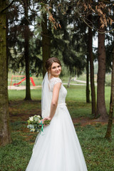 Fototapeta na wymiar Handsome gorgeous bride in white wedding dress with bridal bouquet