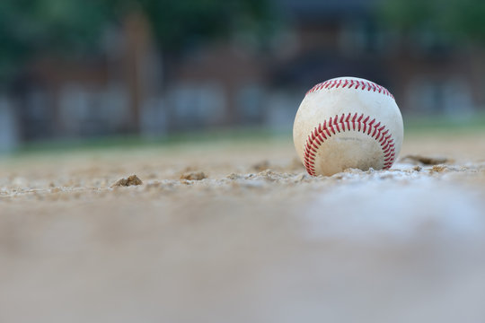 A baseball sits right on the foul line on a sandy baseball field