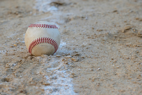 Baseball sits on the foul line on sandy lot