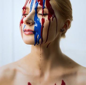 Paint on the female face, close-up. Flows of red and blue paint on the face. Art portrait of a hard face in paint.