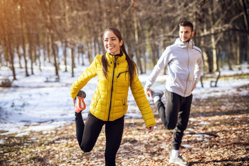 Portrait view of young happy attractive beautiful smiling fitness sporty couple in winter sportswear warming in the snowy forest.