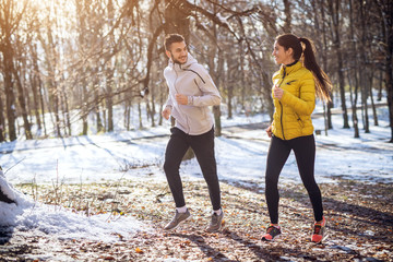 Side view of young happy charming smiling fitness sporty couple in winter sportswear jogging in the...