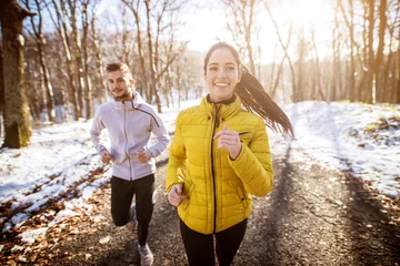Photo sur Plexiglas Jogging Portrait view of young happy cute charming adorable fitness shape girl in winter sportswear jogging in the snowy forest with her boyfriend or trainer.