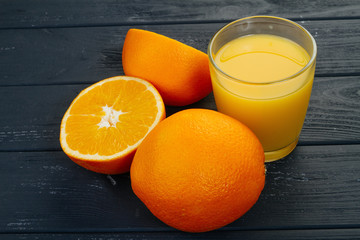 Glass of orange juice and orange on grey background.