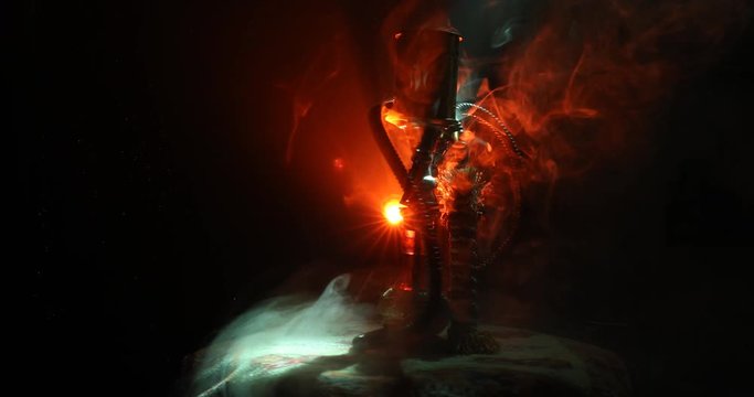 Hookah hot coals on shisha bowl on orange (like fire) clouds of steam on dark background. Stylish oriental shisha. Shisha Concept. On rotating display. 