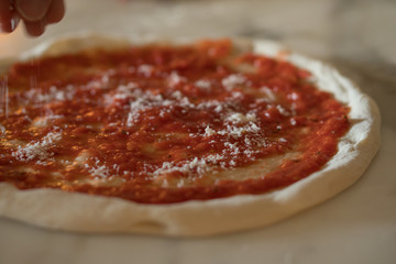 tomato based pizza being topped with cheese