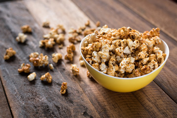 caramel popcorn in a yellow bowl on a wooden table background. popcorn in a bowl and scattered on table
