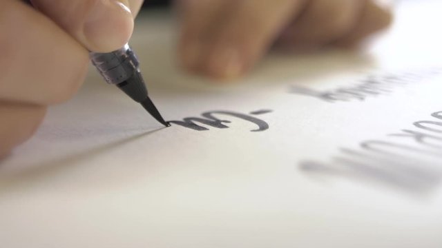 The hand holds the pen and brush and prints the word on paper.