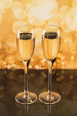 Two glasses of champagne with golden light bokeh on background.