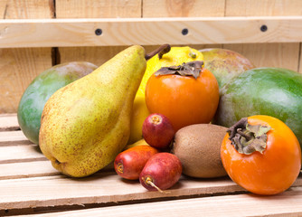 Ripe fresh organic fruits on the wooden background. Mango, pear, kiwi, dates, lenom, persimmon. Fruit on the wooden box. Top view.