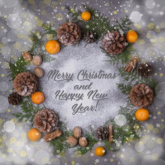 Merry Christmas and Happy New Year background. Christmas wreath with snow fir cones tangerines spruce cinnamon nuts. Flat lay. Copy space. Snow and light effect boke. Holidays lettering.
