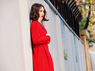 Fototapeta premium Beautiful young brunette woman wearing a red coat in autumn city. Outdoor fashion portrait of glamour young Chinese cheerful stylish lady in street. Emotions, people, beauty and lifestyle concept.