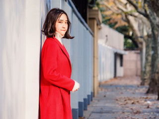 Beautiful young brunette woman wearing a red coat in autumn city. Outdoor fashion portrait of glamour young Chinese cheerful stylish lady in street. Emotions, people, beauty and lifestyle concept.