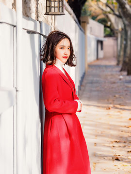 Beautiful young brunette woman wearing a red coat in autumn city. Outdoor fashion portrait of glamour young Chinese cheerful stylish lady in street. Emotions, people, beauty and lifestyle concept.