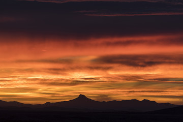very intense orange and yellow sunrise with layered clouds over a beautiful mountain