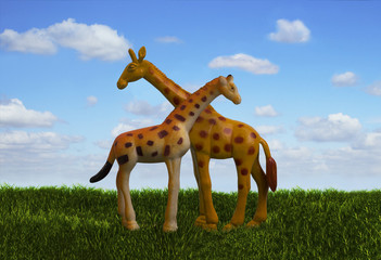 Two giraffes toys with necks crossed standing on the meadow with green grass and blue cloudy sky. Side view.