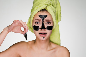a frustrated girl with a towel on her head takes off the cleansing mask