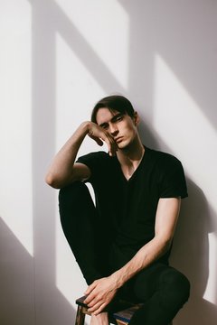 Vertical portrait of young handsome brunet in contrast lightning  and his shadow on white wall